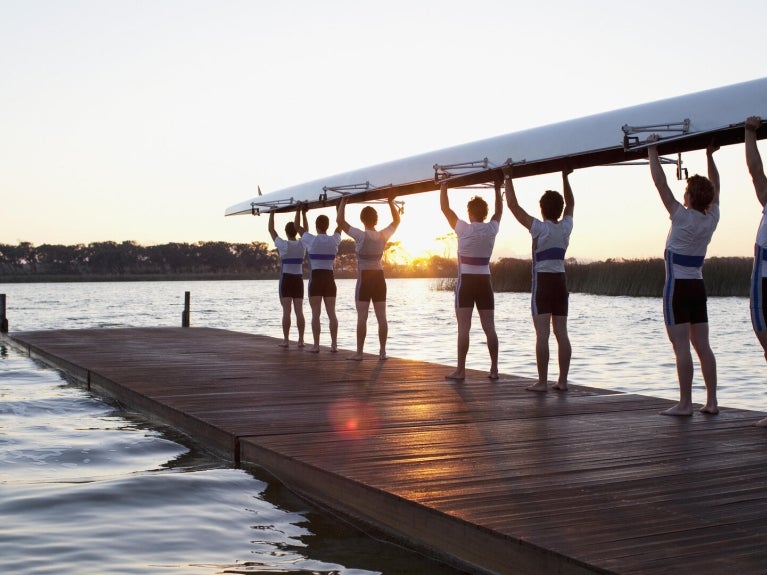 Rowing team holding up boat at sunrise